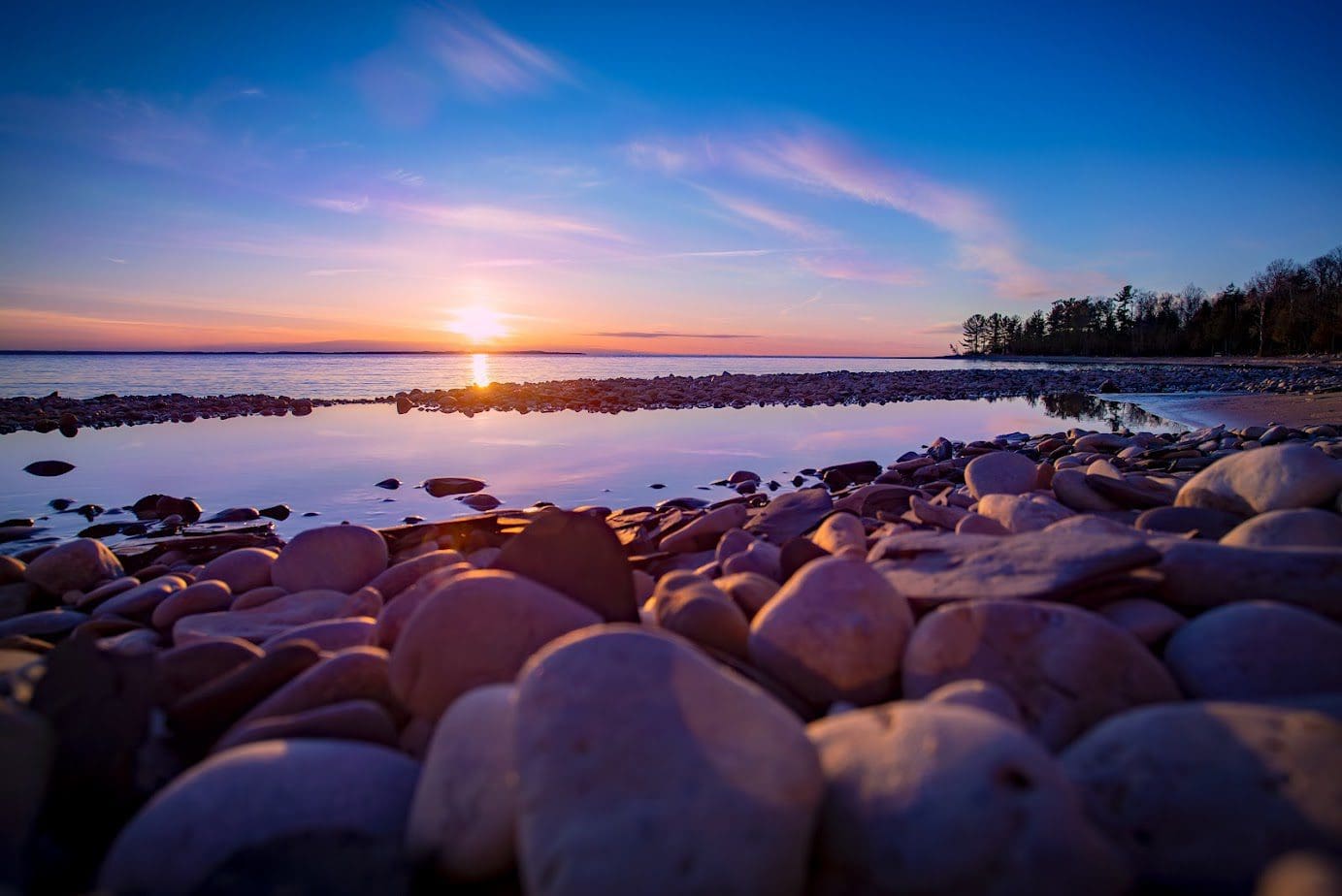 Rocky shoreline at sunset with colorful sky.
