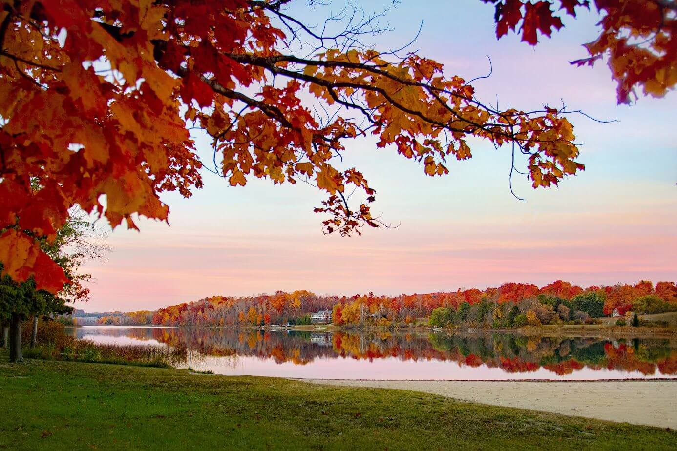 Autumn trees with colorful leaves reflecting on a calm lake at sunset.
